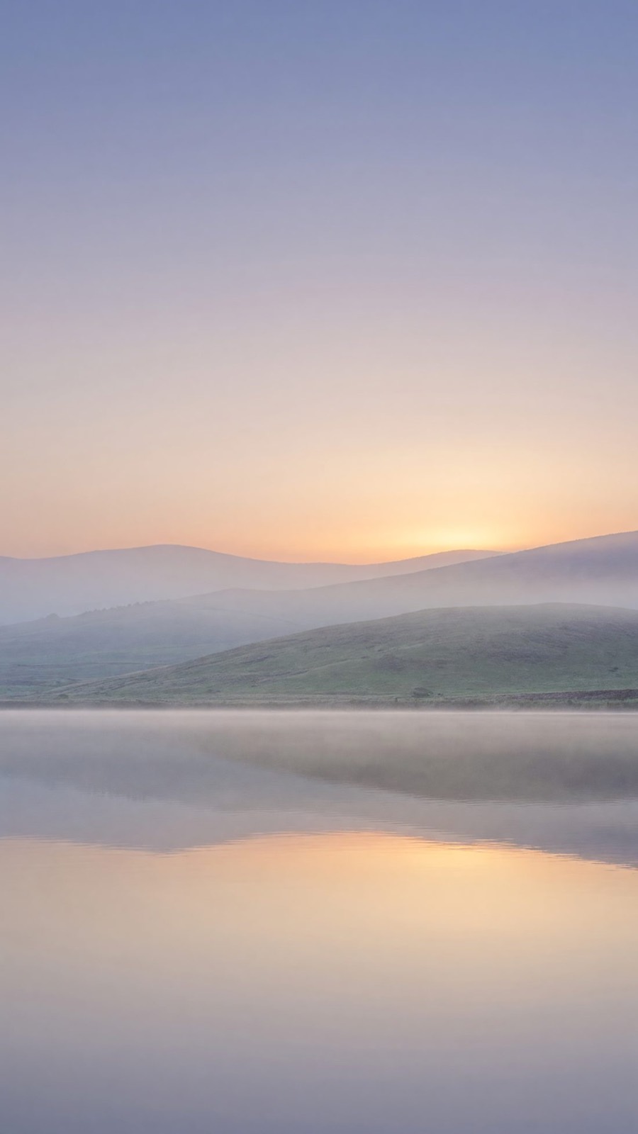 Sunrise over misty hills and a still lake.